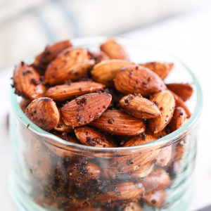 this is a close up shot of homemade roasted spiced almonds glistening with their coating, and sitting in a clear glass bowl