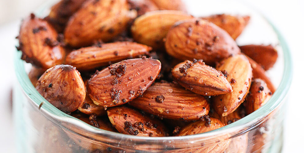 this is a close up shot of homemade roasted spiced almonds glistening with their coating, and sitting in a clear glass bowl