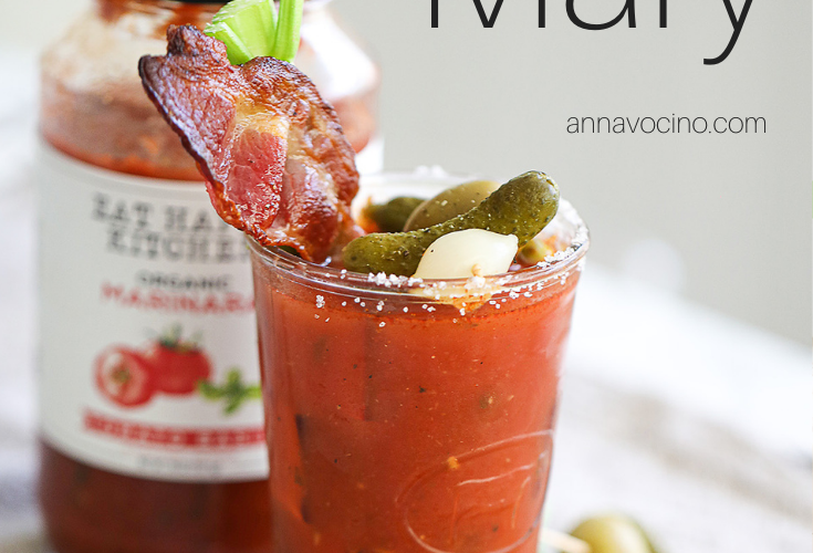 this is a PIN for Pinterest of the the bacon Bloody Mary with celery and bacon garnished glass of bloody Mary cocktail with a jar of Eat Happy Marinara behind it